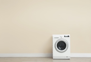Photo of Washing machine near color wall in empty room, space for text. Laundry day