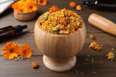 Photo of Mortar of dry calendula flowers on wooden table