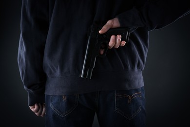 Photo of Man holding gun behind his back on black background, closeup