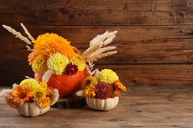 Decorative pumpkins with beautiful flowers and spikelets on wooden table. Space for text