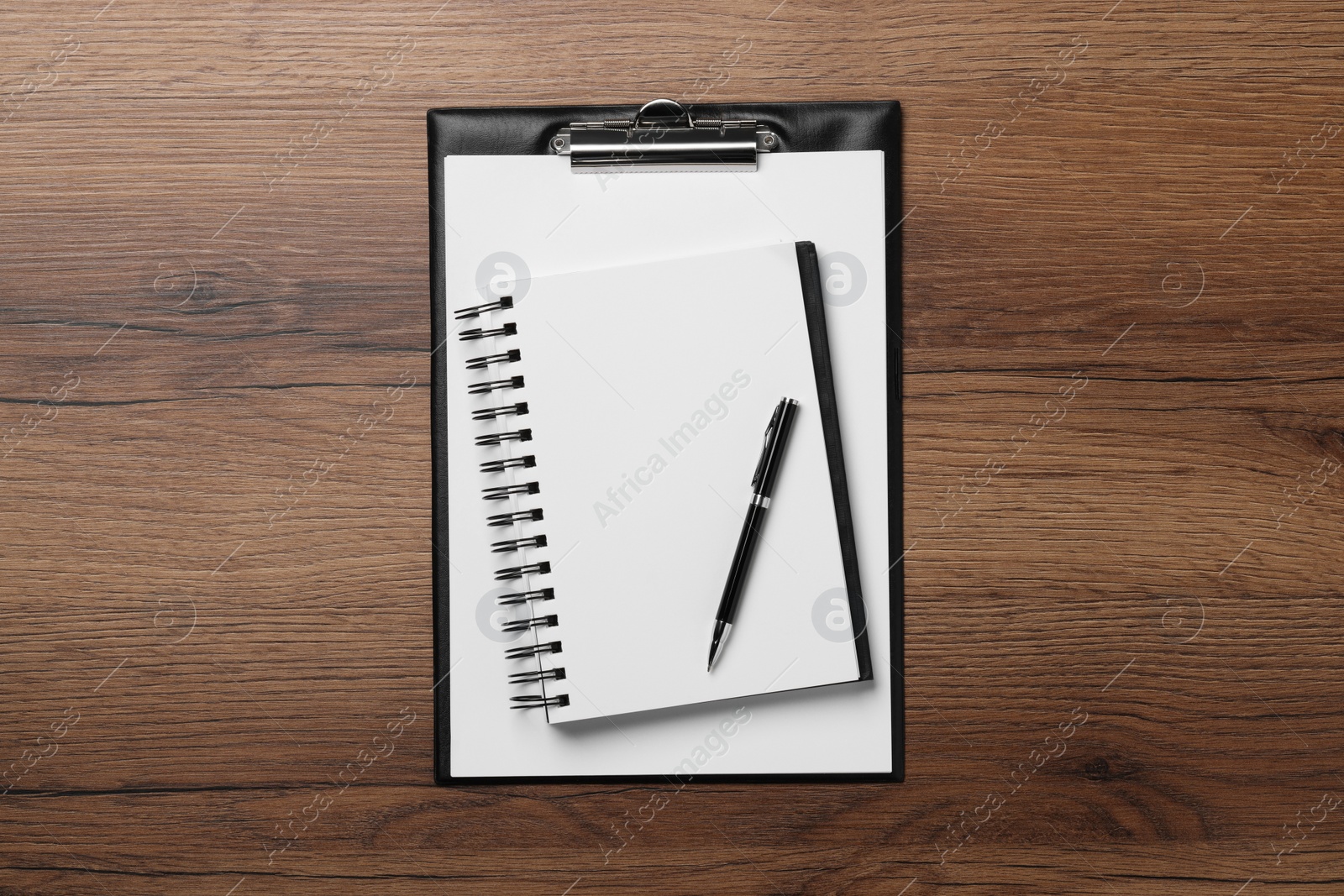 Photo of Ballpoint pen, notebook and clipboard with paper sheet on wooden table, flat lay
