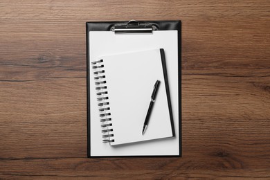 Ballpoint pen, notebook and clipboard with paper sheet on wooden table, flat lay