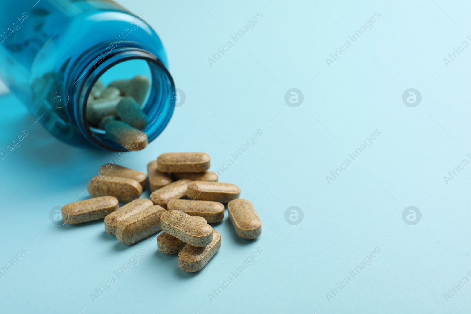 Photo of Overturned bottle with dietary supplement pills on light blue background, closeup. Space for text