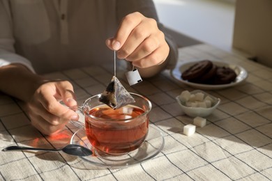 Woman taking tea bag out of cup at table indoors, closeup