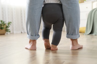 Mother supporting her baby daughter while she learning to walk at home, closeup