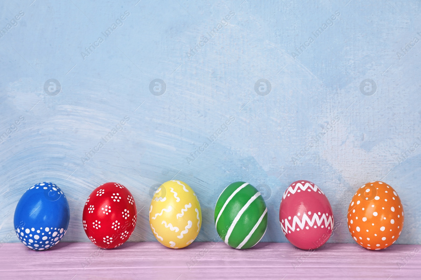 Photo of Decorated Easter eggs on table near color wall. Space for text