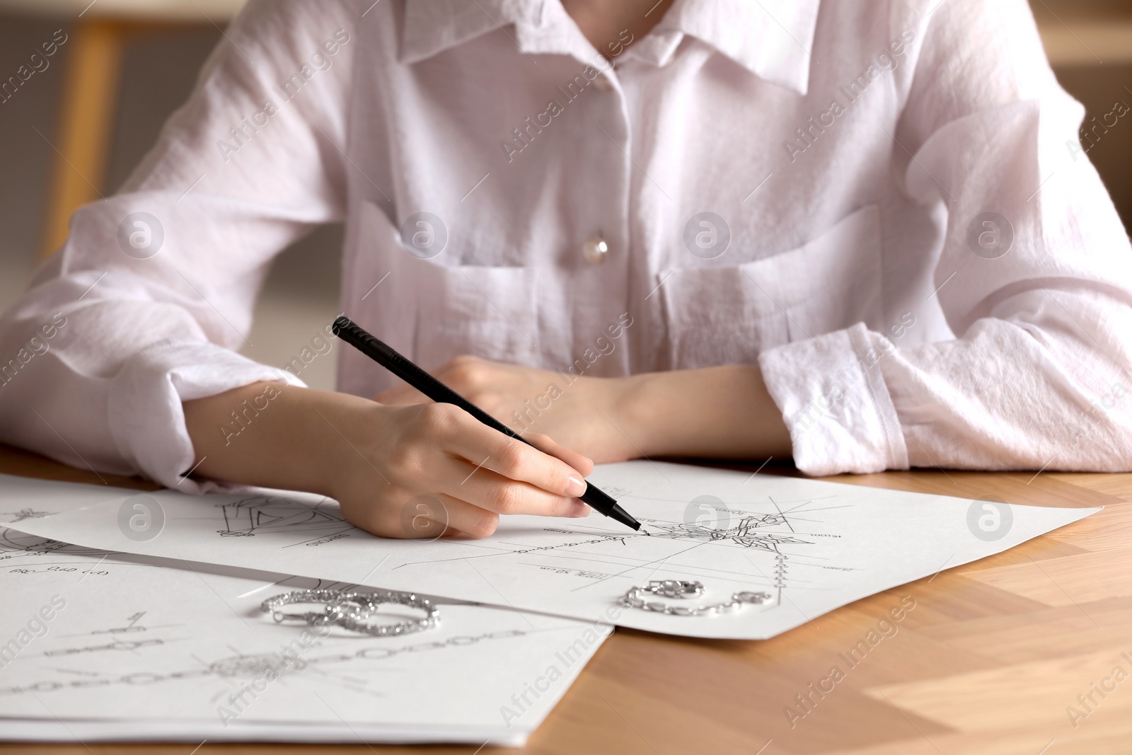 Photo of Jeweler drawing sketch of elegant necklace on paper at wooden table indoors, closeup
