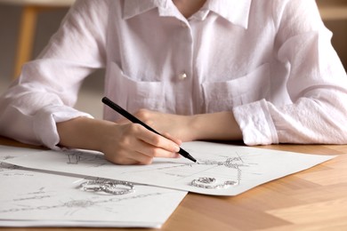 Jeweler drawing sketch of elegant necklace on paper at wooden table indoors, closeup