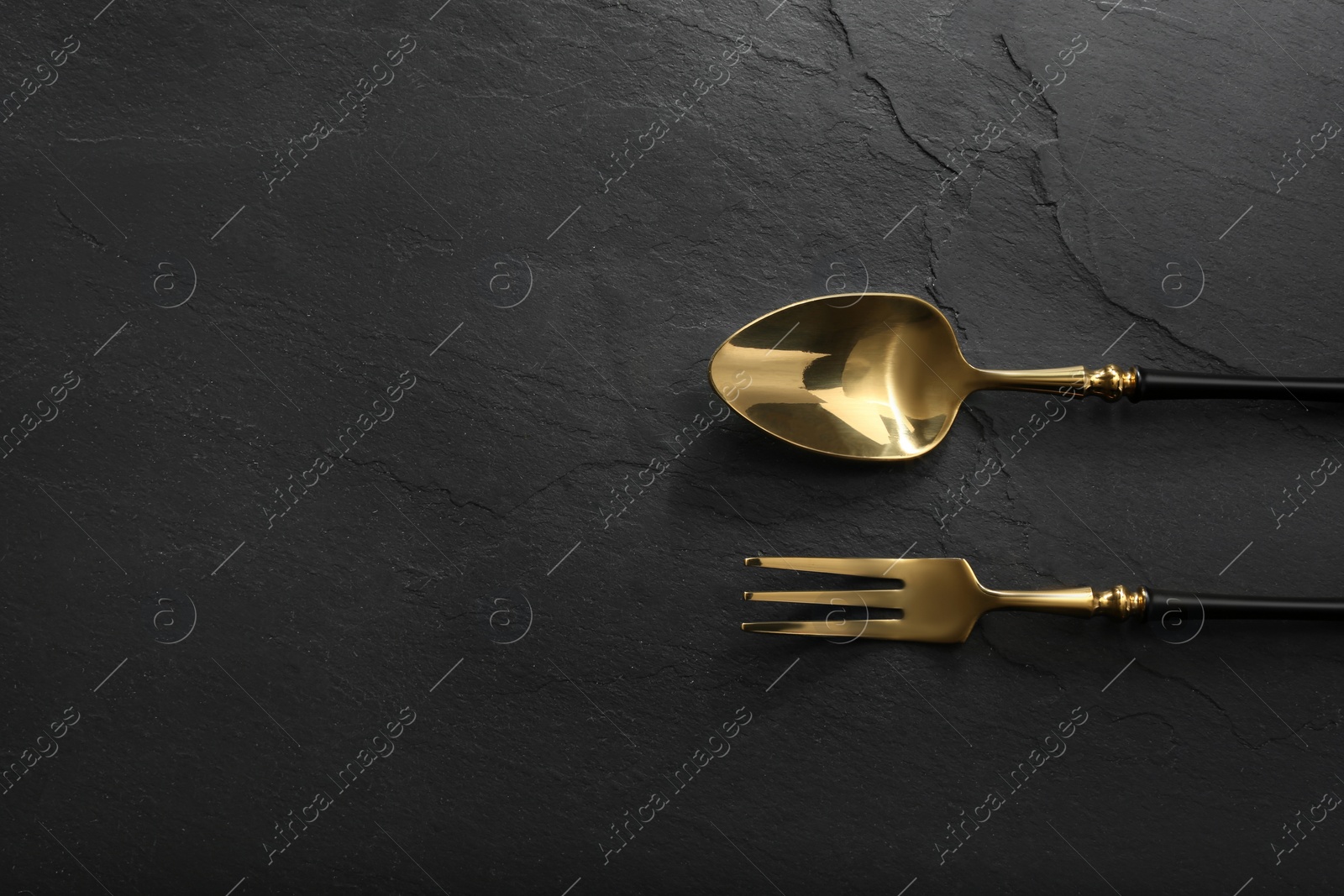 Photo of Shiny fork and spoon on black table, flat lay. Space for text