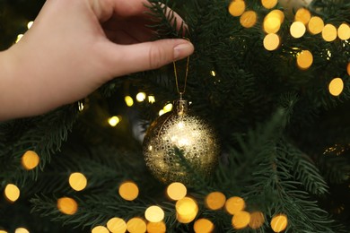 Photo of Woman decorating fir tree with golden Christmas ball, closeup