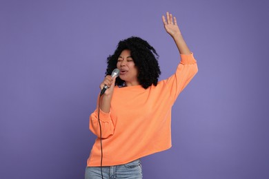 Beautiful woman with microphone singing on violet background