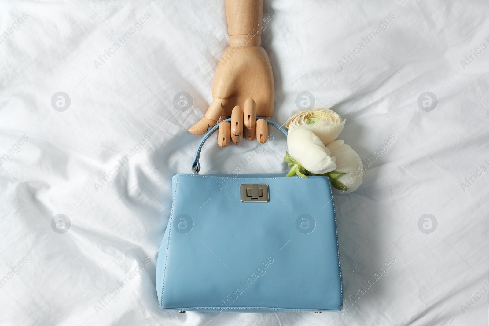 Photo of Stylish bag with spring flowers and wooden mannequin hand on crumpled sheet, flat lay