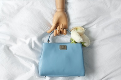 Photo of Stylish bag with spring flowers and wooden mannequin hand on crumpled sheet, flat lay