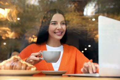 Special Promotion. Happy young woman with cup of drink using laptop in cafe, view from outdoors