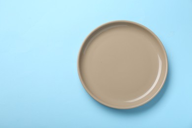 Photo of Empty beige ceramic plate on light blue background, top view. Space for text