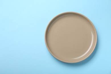 Empty beige ceramic plate on light blue background, top view. Space for text