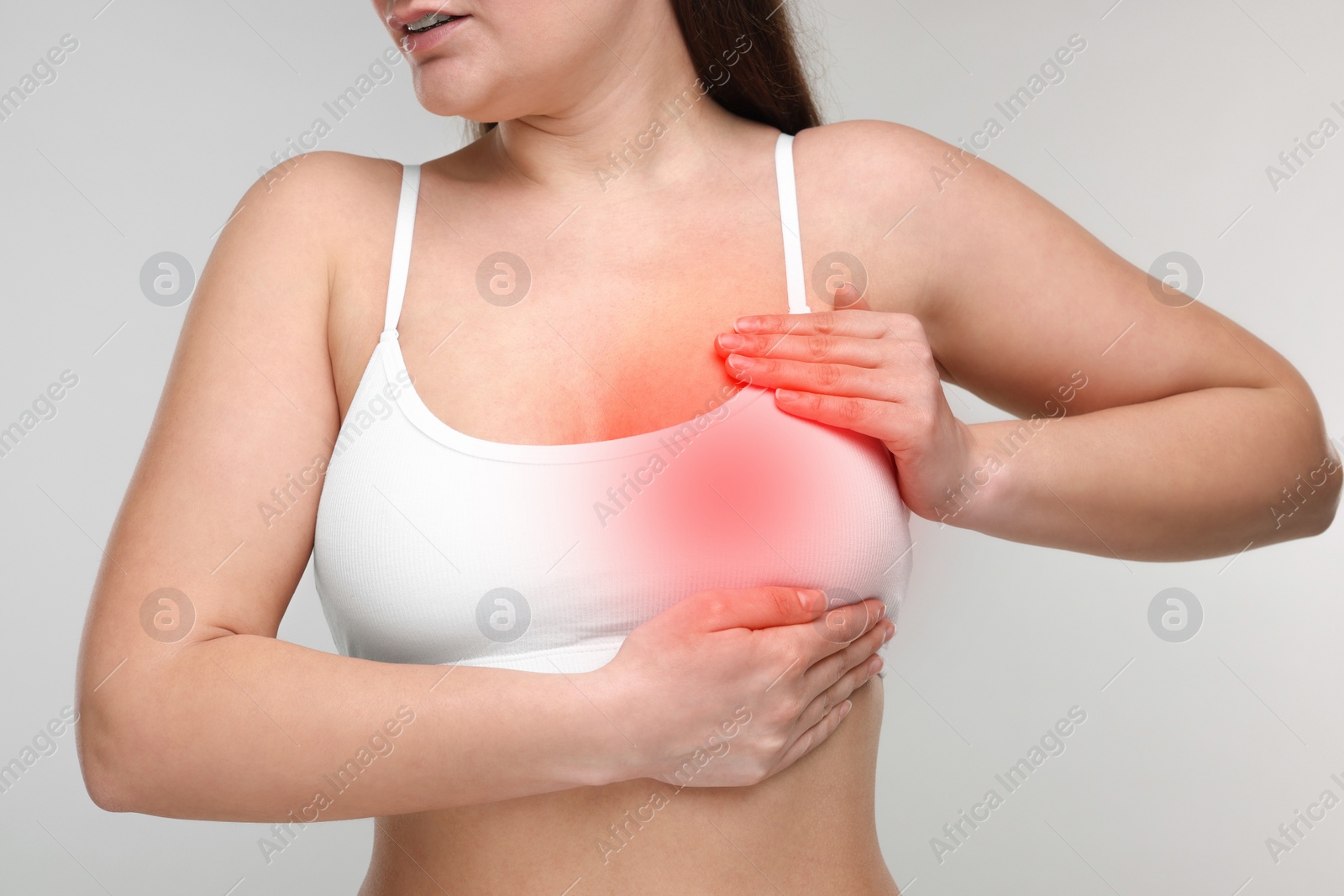 Image of Young woman suffering from breast pain on light grey background, closeup