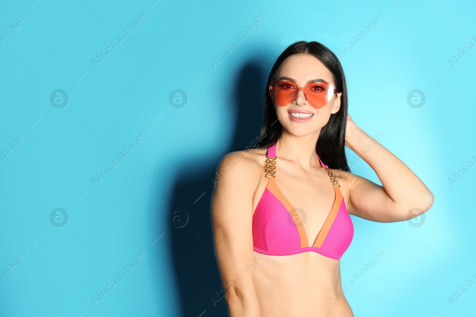 Photo of Beautiful young woman in stylish bikini with sunglasses on light blue background. Space for text