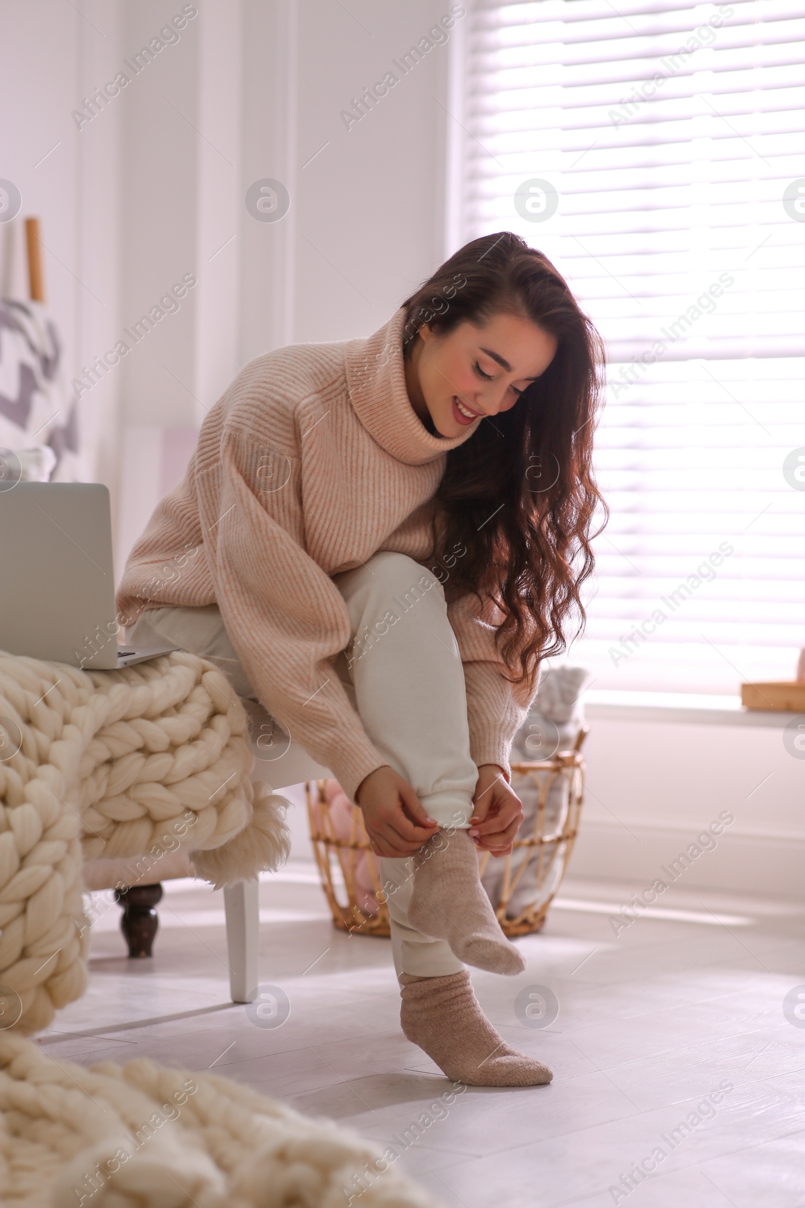 Photo of Beautiful young woman putting on socks at home. Cozy atmosphere