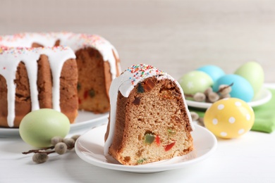 Piece of glazed Easter cake with sprinkles and painted eggs on white wooden table