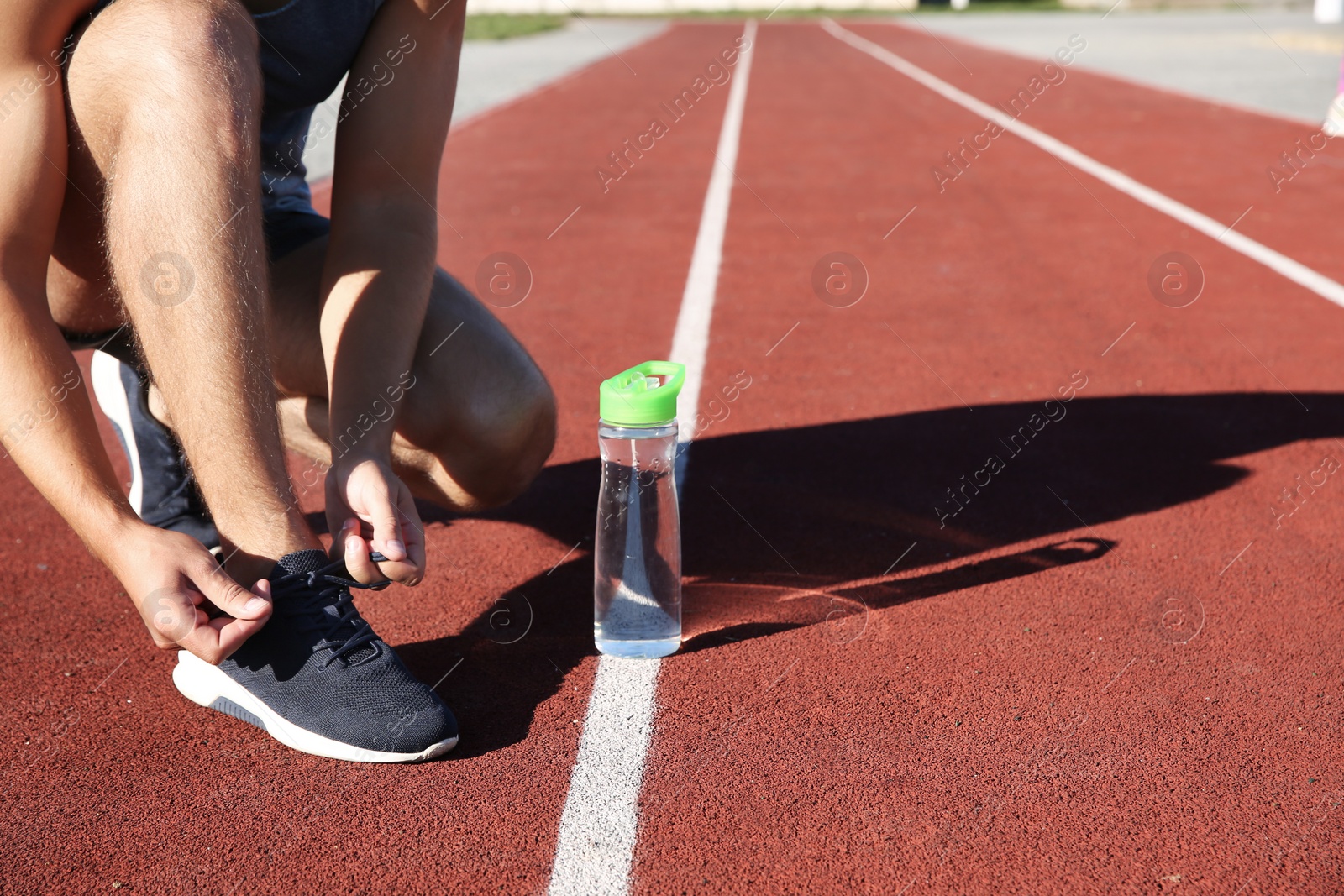 Photo of Sporty man tying shoelaces before running at stadium on sunny morning