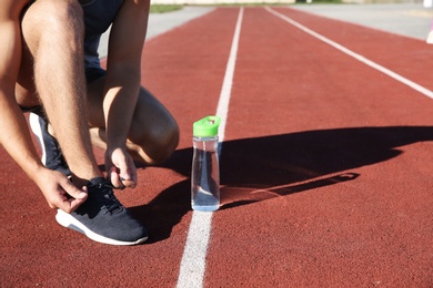 Sporty man tying shoelaces before running at stadium on sunny morning