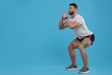 Photo of Young man exercising with elastic resistance band on light blue background. Space for text