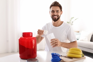 Photo of Young man preparing protein shake at table in room