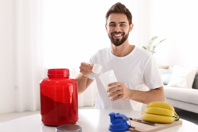 Young man preparing protein shake at table in room