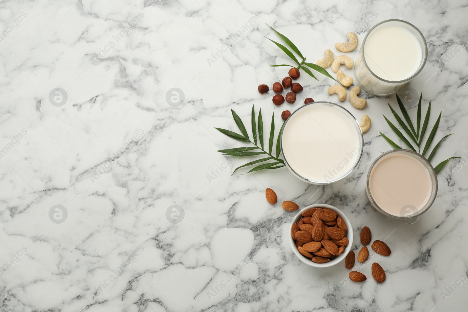 Photo of Different vegan milks and ingredients on white marble table, flat lay. Space for text