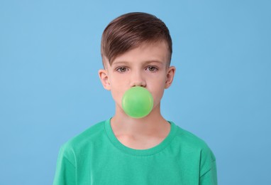 Photo of Boy blowing bubble gum on light blue background
