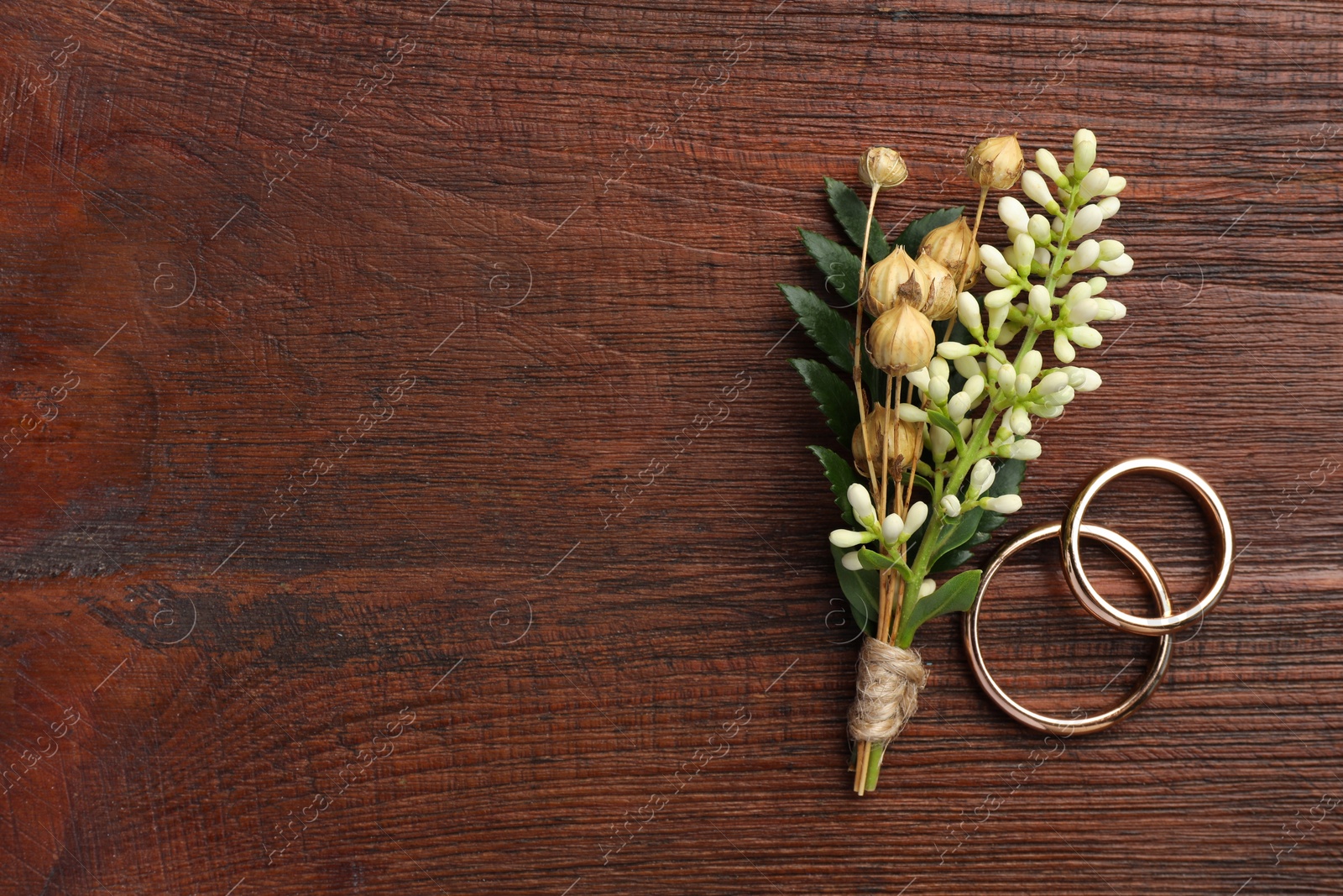Photo of Small stylish boutonniere and rings on wooden table, top view. Space for text