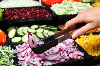 Photo of Young woman taking fresh red onion from salad bar, closeup