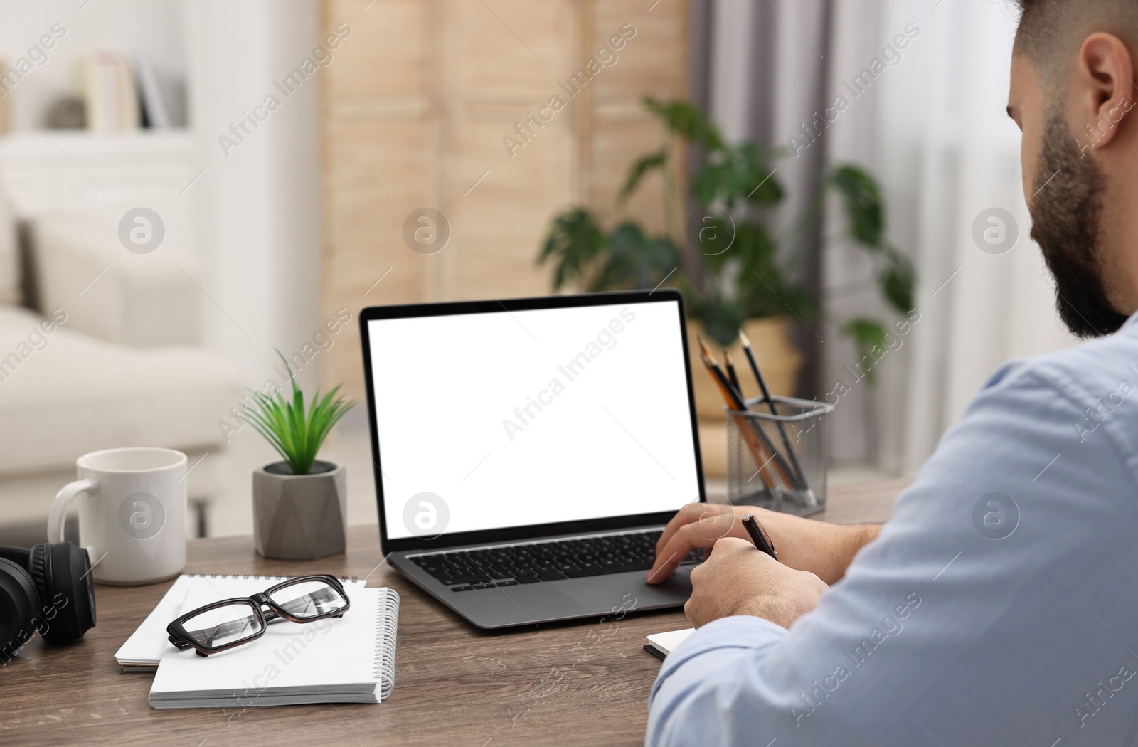 Photo of E-learning. Young man using laptop at wooden table indoors, closeup