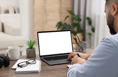 E-learning. Young man using laptop at wooden table indoors, closeup