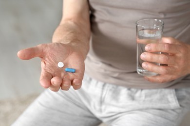 Photo of Senior man with pills and glass of water indoors, closeup