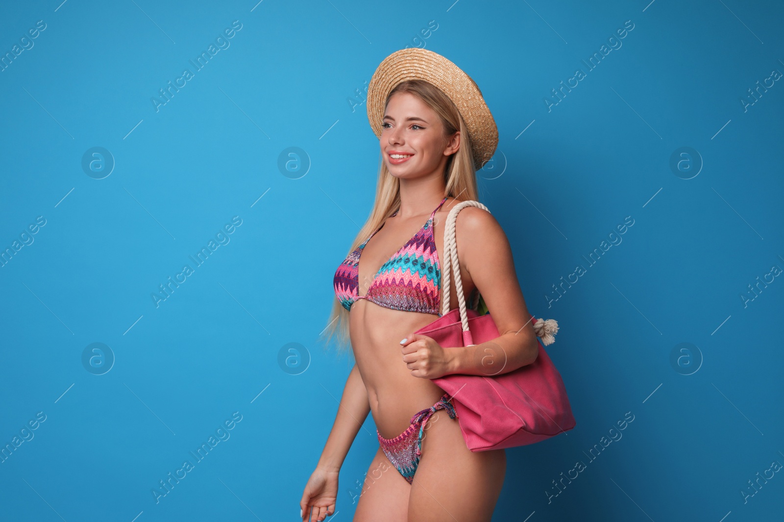 Photo of Pretty young woman wearing stylish bikini with bag on blue background