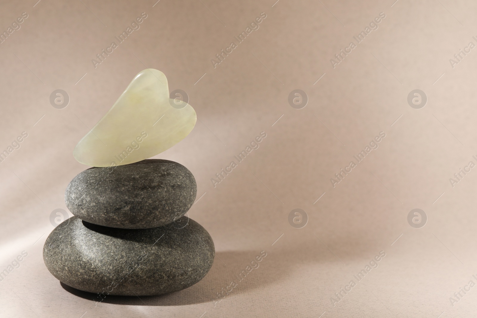 Photo of Jade gua sha tool and spa stones on brown background, space for text