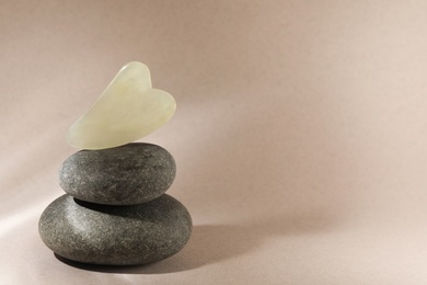 Photo of Jade gua sha tool and spa stones on brown background, space for text