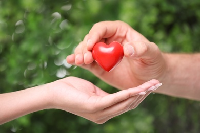 Photo of Man giving red heart to woman on blurred green background, closeup. Donation concept