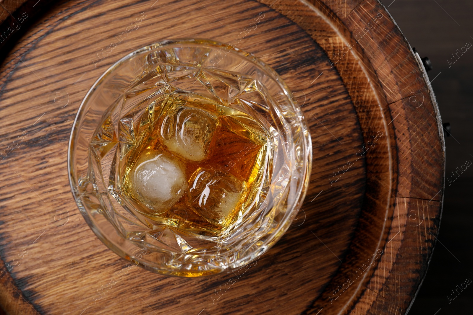 Photo of Glass of tasty whiskey on wooden barrel, top view