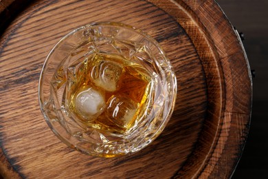 Glass of tasty whiskey on wooden barrel, top view