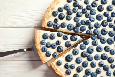 Tasty cake with blueberry and pie server on wooden table, top view