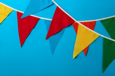 Photo of Buntings with colorful triangular flags on light blue background. Festive decor