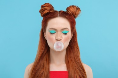 Photo of Beautiful woman with bright makeup and closed eyes blowing bubble gum on light blue background