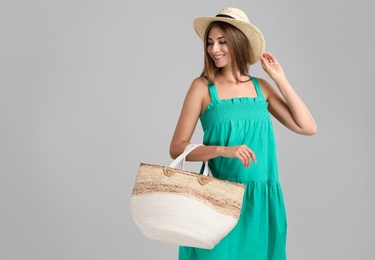 Photo of Beautiful young woman with stylish straw bag on light grey background. Space for text