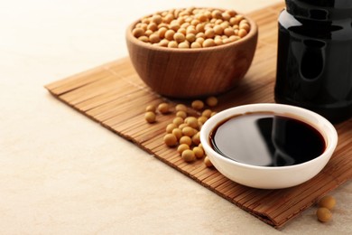 Photo of Soy sauce in bowl and soybeans on beige table, space for text