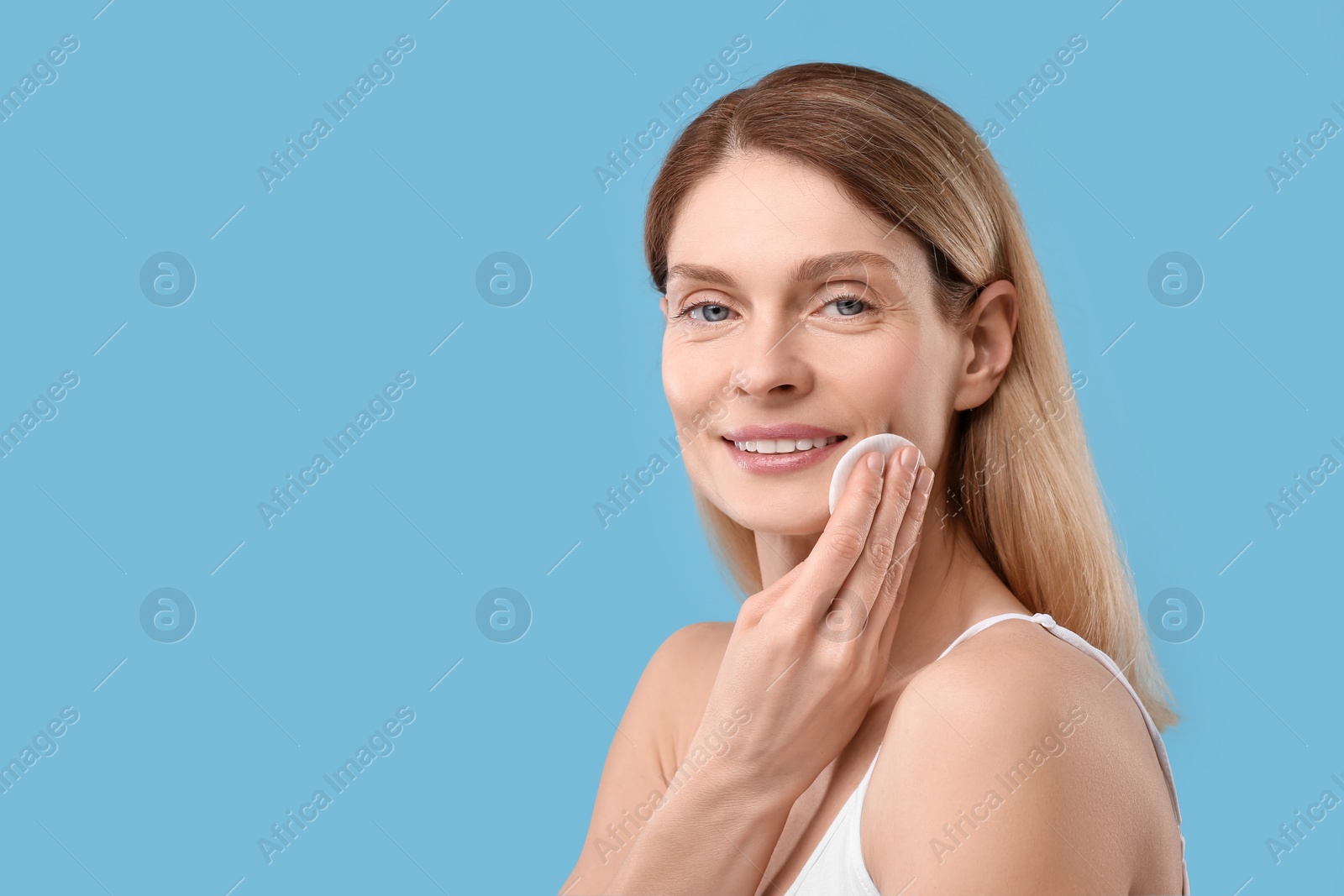 Photo of Beautiful woman removing makeup with cotton pad on light blue background, space for text