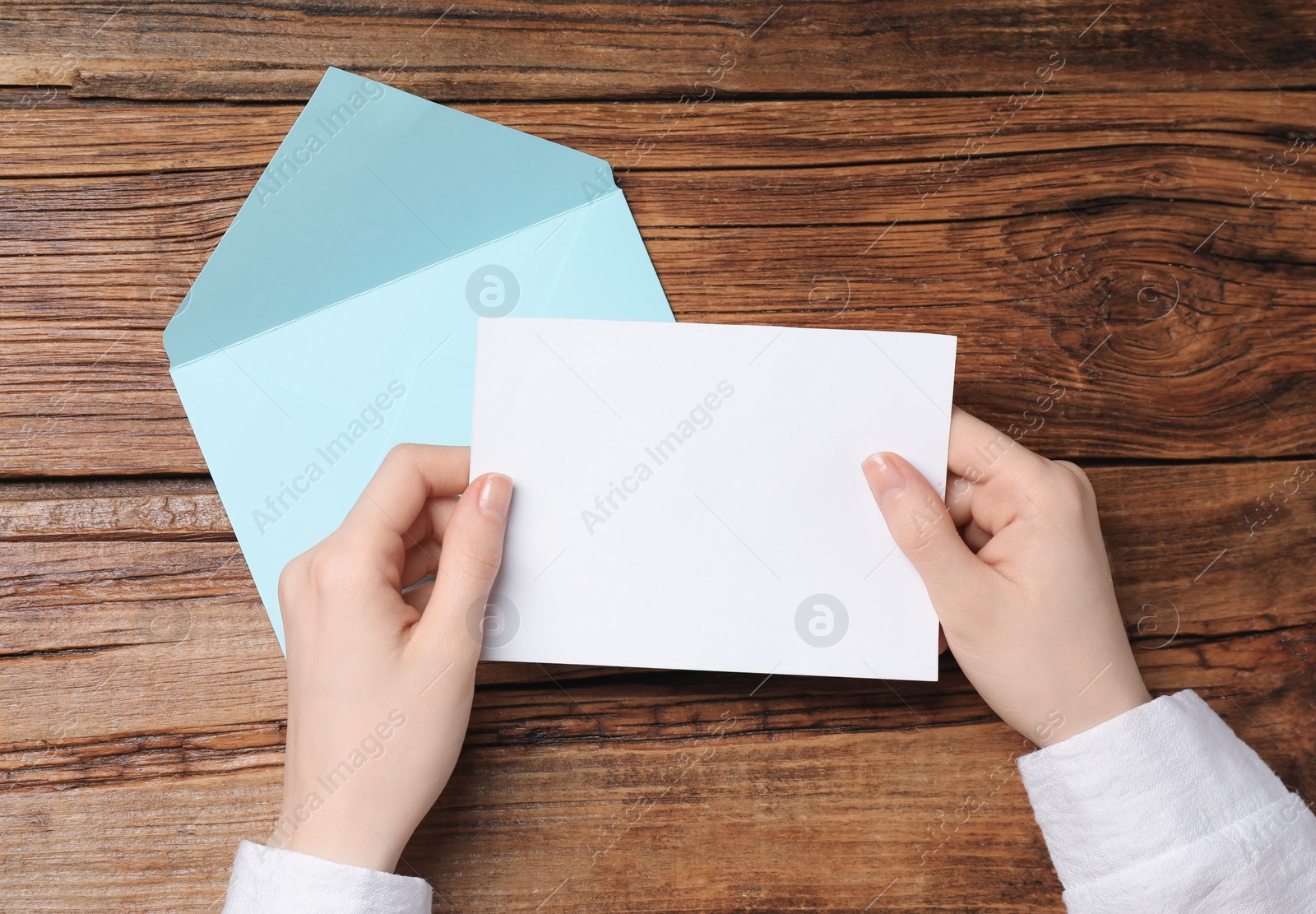 Photo of Woman with blank card at wooden table, top view. Space for text