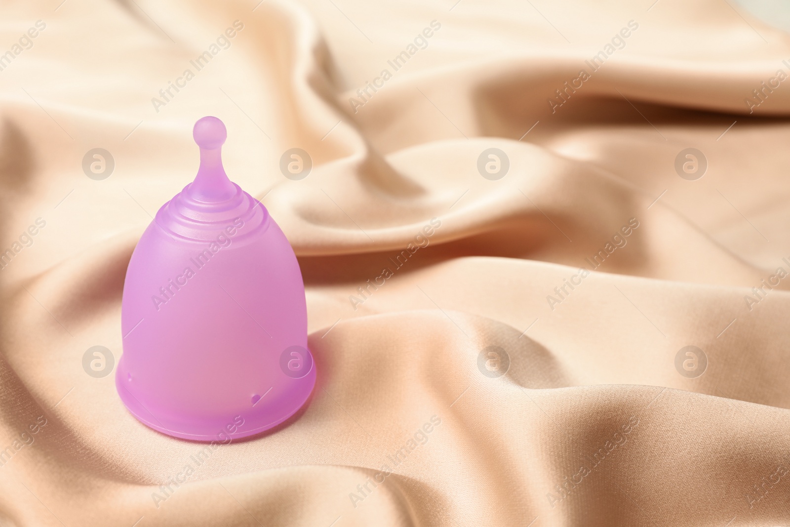 Photo of Menstrual cup on beige silk fabric. Space for text